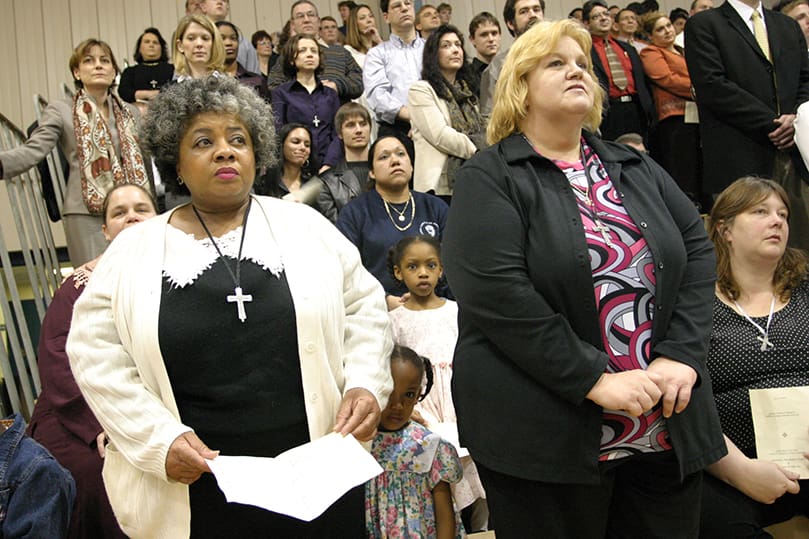 Valerie Calloway, left, and Cynthia Lee, stand during the presentation of the candidates. The women represent two of the 76 candidates at St. Lawrence Church, Lawrenceville. Some 478 catechumens and 950 candidates from 40 parishes attended the Feb. 13 Rite of Election and Call to Continuing Conversion at St. Pius X High School, Atlanta. Photo by Michael Alexander