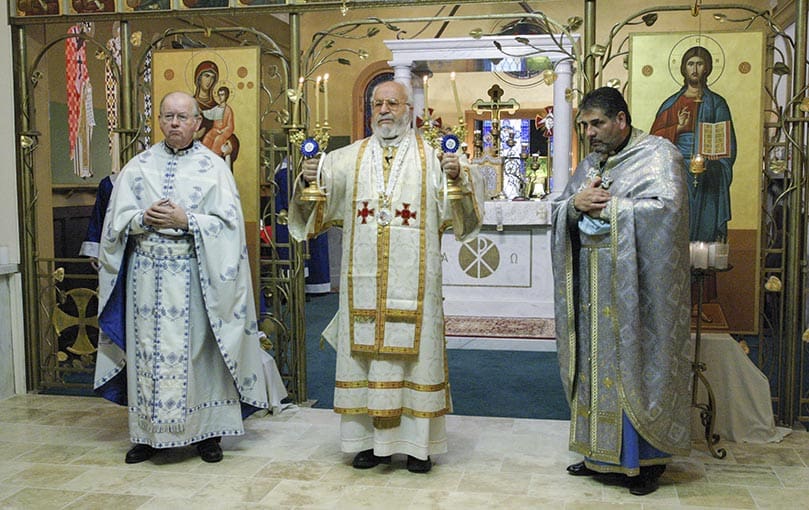 Flanked by Father Tom Flynn of Emory University, left, and Father John Azar, pastor of St. John Chrysostom Melkite Church, Archbishop Cyril Salim Bustros, center, gives a final blessing to the congregation at the conclusion of the hierarchical liturgy, Feb. 19. The three candles in his right hand symbolize the Trinity and the two candles in his left hand symbolize the dual nature of Christ as divine and human. Photo By Michael Alexander