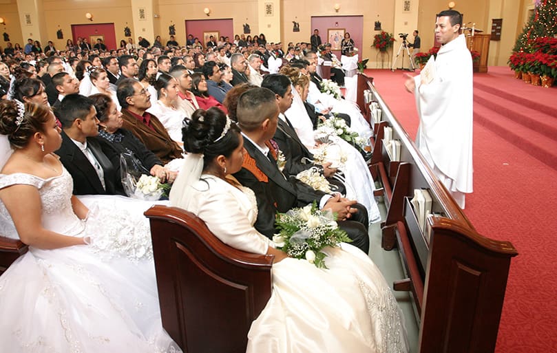 Father Jesús-David Trujillo, right, pastor of St. Joseph Church, Dalton, stands before the couples as he delivers his homily. He worked with the couples six to eight months during the marriage preparation process. Photo By Michael Alexander