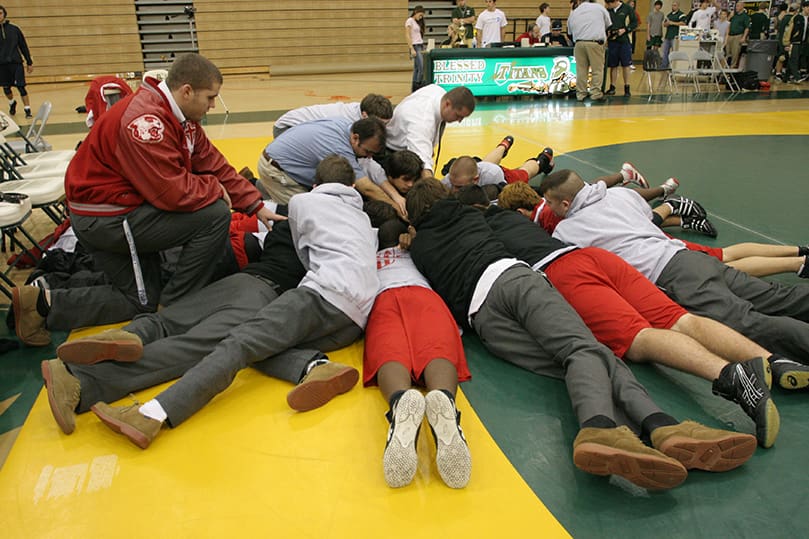 Our Lady of Mercy High School head wrestling coach Francis Giknis, background center, fired up his wrestling team before their second round of matches during the Jan. 8 Catholic Duals. Here the team continues to gather around the coach for a team prayer. Photo By Michael Alexander