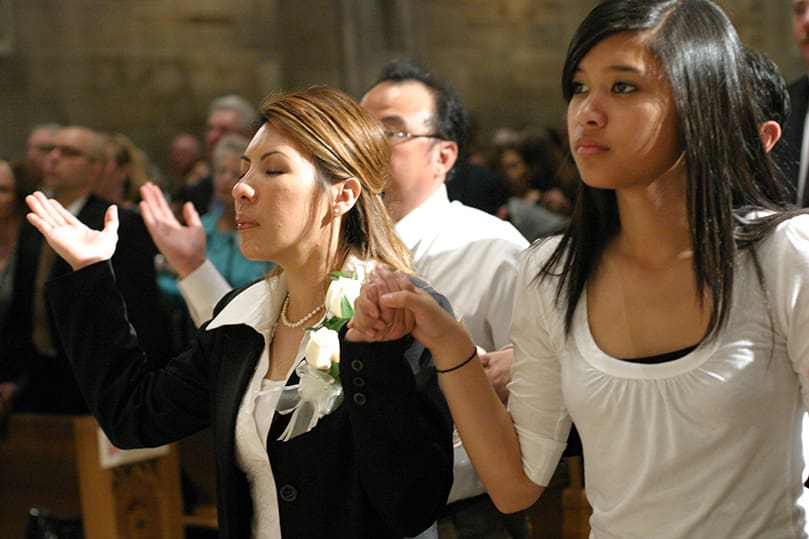 Yesica Anugerah, the wife of ordained permanent deacon Antonius, joins hands with her 15-year-old daughter Audrey during The Our Father. Deacon Anugerah will serve the Indonesian community at Our Lady of the Assumption Church, Atlanta. Photo By Michael Alexander