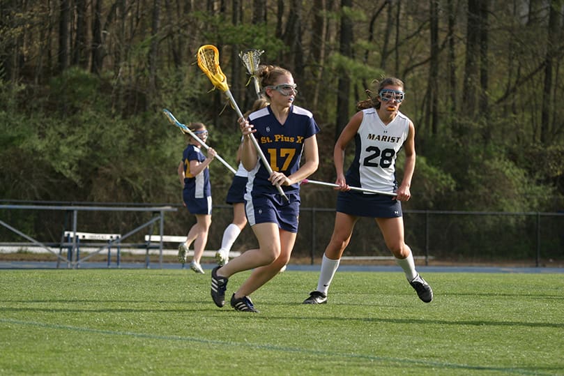 St. Pius X senior Emma Kelly (#17) cradles the ball in her stick as she moves in for the attack around Marist center Valerie McKeon (#28). St. Pius was defeated in the April 2 lacrosse match 12-6. Photo By Michael Alexander