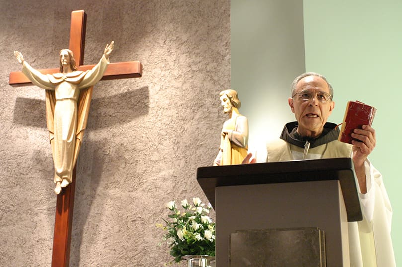 Holding the worn New American Bible he brought to the Georgia Tech 38 years ago, Father DiLella, OFM, preaches his final Sunday homily from the pulpit of the Georgia Tech Catholic Center, April 27. Photo By Michael Alexander