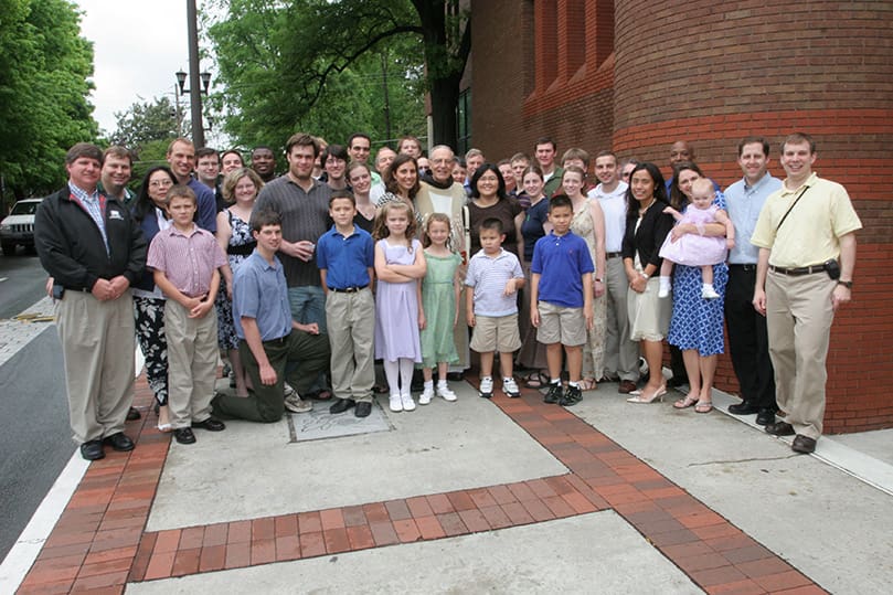 Past and present students, parents of students and children of former students surround Father Mario DiLella, OFM, second row, center, as they pose for a photograph outside the Catholic Center at Georgia Tech. Photo By Michael Alexander
