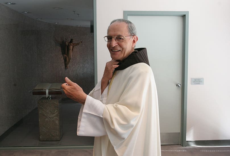 Father Mario DiLella, OFM, looks back toward the front door as he holds his watch in his hand. The 81-year-old priest is a stickler for time as he prepares to celebrate the 5:30 p.m. Mass. Photo By Michael Alexander