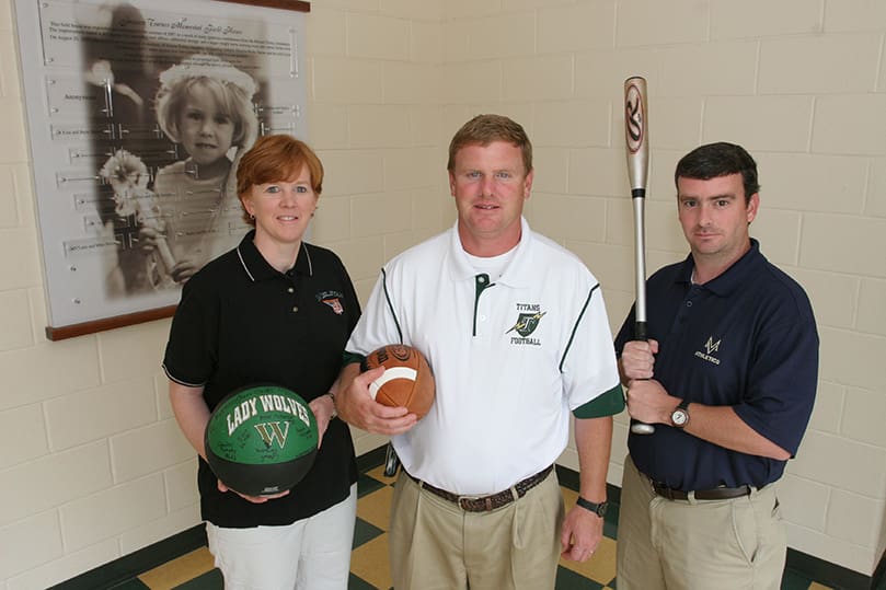 Ricky Turner, center, stands with his sister Jan Azar, left, and his brother Mike in the field house at Blessed Trinity High School, Roswell, named after his late daughter Jessica Nicole Turner (photo in background). Ricky is the head football coach and athletic director at Blessed Trinity, Jan is the girls basketball coach and assistant athletic director at Wesleyan School, Norcross, and Mike is the head baseball coach at Mount Vernon Presbyterian School, Atlanta. Photo By Michael Alexander