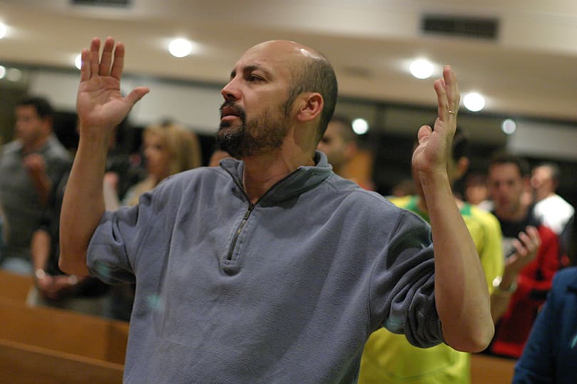 Jose Antonio Xavier Mendes raises his hands during a moment of fervent prayer as the Brazilian community celebrates Mass at Holy Family Church. Photo By Michael Alexander