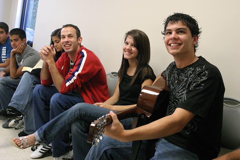 (R-l) Acoustic guitar player and youth leader Angelo Dona laughs with Fernanda Martins and Daniel Rocha during a gathering of Brazilian youth before Sunday liturgy, Oct. 19. Photo By Michael Alexander