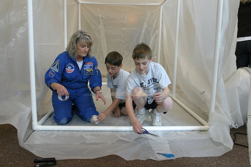 On the second day of the Build-A-Shuttle project Linda Taylor, an educator with the U.S. Space and Rocket Center, Huntsville, Ala., works with second-graders Bret Madren, center, and Joseph Nicholson as they put the floor down in the orbiter. Photo By Michael Alexander