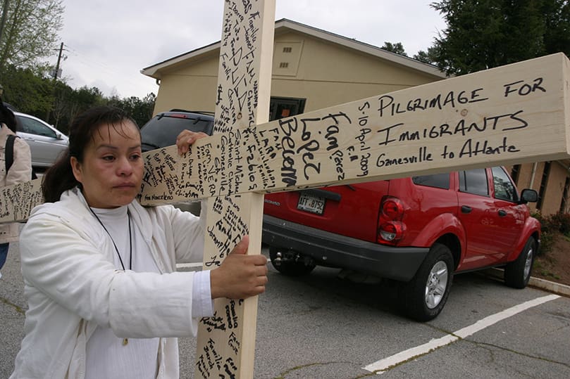 Laura Ramirez leads off the pilgrimage carrying a cross with the names of participants, detainees and prayers. Immigrants in Gainesville made the cross as a gift to the pilgrimage. Photo By Michael Alexander