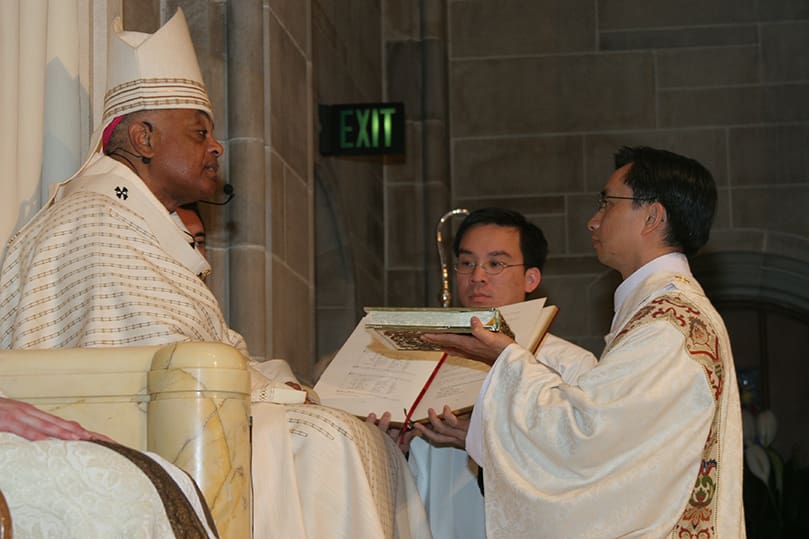 Thang Minh Pham, right, receives the Book of Gospels from the Archbishop Gregory. Photo By Michael Alexander