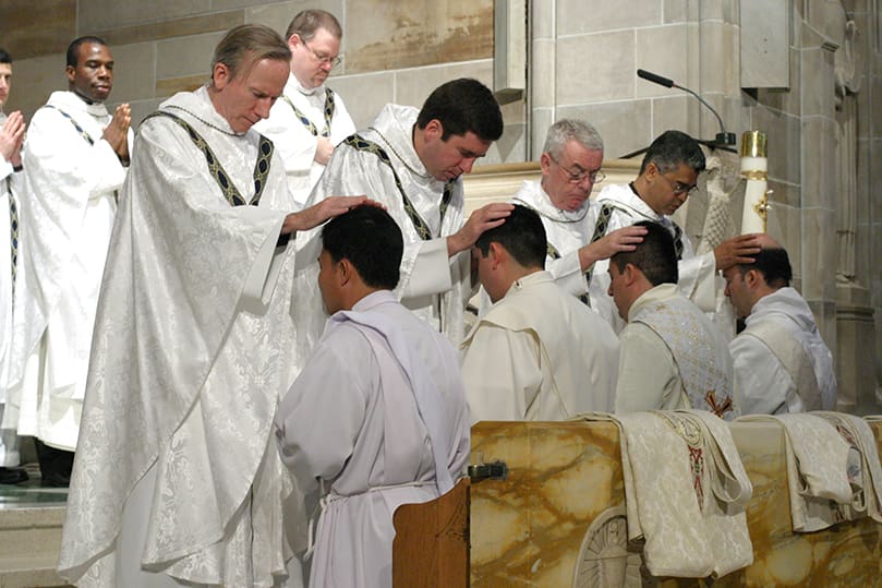 (L-r, standing) Father Neil J. Herlihy, pastor of Saint Peter the Rock Church, The Rock, Father Joseph Shaute, pastor of Saint Clement Church, Calhoun, Father John Fallon, prison chaplain, and Father Luis Guillermo Cordoba, administrator of Our Lady of the Americas Mission, Lilburn, lay hands upon ordination candidates (l-r) Dominic Tran, Ignacio Morales, Salomon Garcia Cortes, and Nicholas Azar, respectively. They represent half of the eight men who were ordained to the priesthood on June 27 at the Cathedral of Christ the King, Atlanta. Photo By Michael Alexander