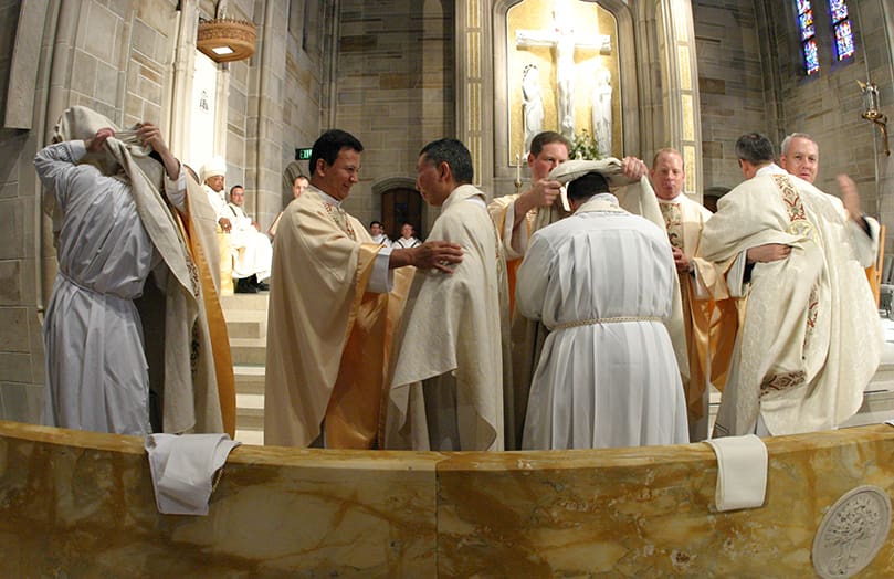 (L-r) During the investiture with stole and chasuble Father Tim Gallagher is assisted by Franciscan of Primitive Observance Father Joseph Paul Medio, Father Fernando Molina Restrepo, pastor of St. Theresa Church, Douglasville, faces Father William Hao, Father Adrian Pleus, pastor of St. Vincent de Paul Church, 	Dallas, helps Father Omar Loggiodice, and Father Brian Higgins, parochial vicar at All Saints Church, Dunwoody, looks on as Father Thomas Hennessy, pastor of Saint Patrick Church, Norcross, gives Father Brian Lorei a congratulatory hug. Photo By Michael Alexander