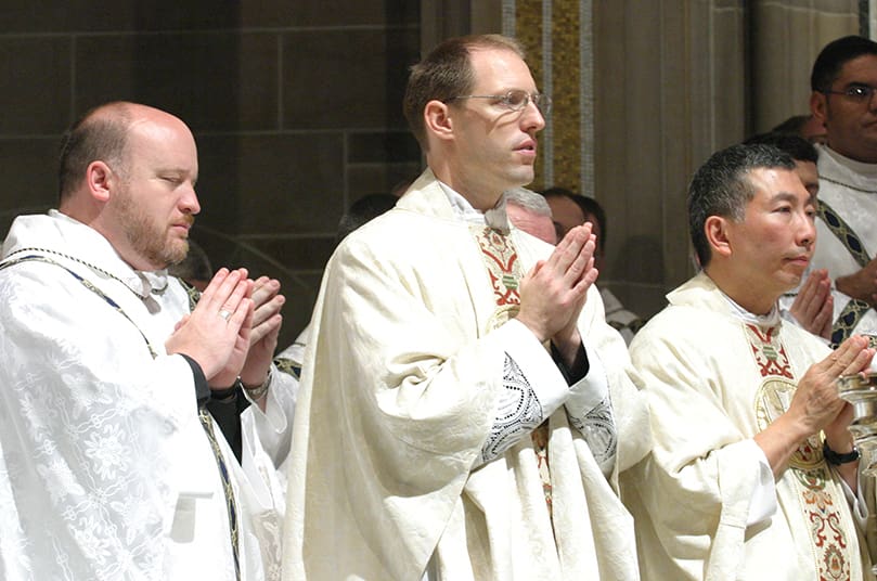 Standing on the Cathedral of Christ the King altar, (l-r) Father Charles Byrd, pastor of Our Lady of the Mountains Church, Jasper, prays beside new priests Father Tim Gallagher and Father William Hao. Photo By Michael Alexander