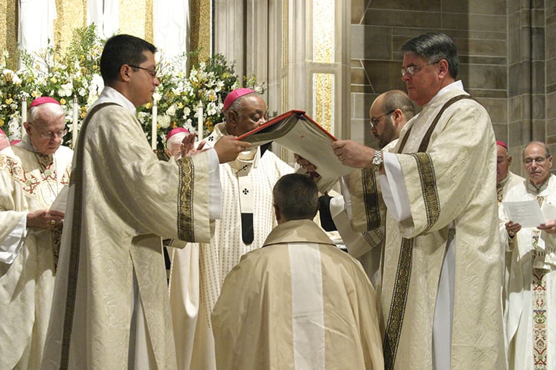 Transitional deacon Mario Lopez, left, and permanent deacon Dennis Dorner hold the Book of the Gospels over Bishop Zarama's head. This moment symbolizes the weight and power of God’s word and the bishop’s responsibility to carry it forth as a teacher.