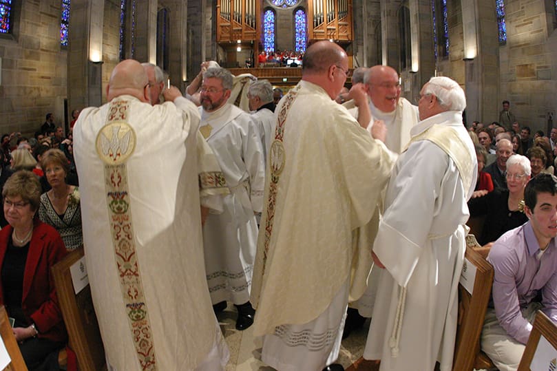 The new deacons and priests gather in the center aisle during the investiture of stole and dalmatic. Photo By Michael Alexander