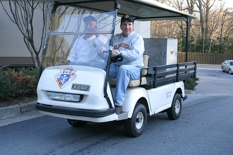 Mike Morris, driving, and Gene Gannon transport the food cooked in the lower kitchen up to the parish hall by way of golf cart. Photo By Michael Alexander