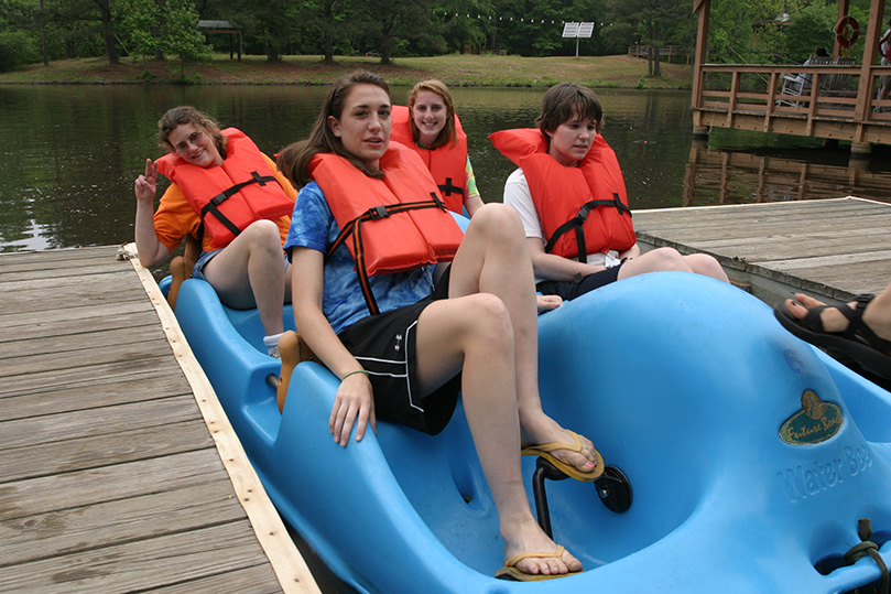 Sitting in a paddle boat, (clockwise from front right) camper Suzanne Feaster, volunteer Olivia Gasper, camper Kimberly Crowe and volunteer Jessica Grant prepare to set out onto Lake Selig, the camp’s upper lake. Photo By Michael Alexander