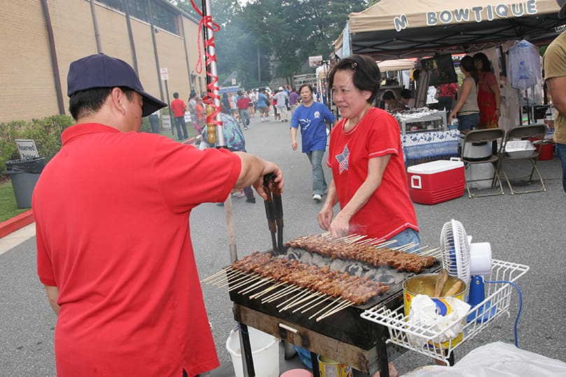 Winata Oei, left, and Lany Wijaya stand over the grill as they cook pork satay. Photo By Michael Alexander