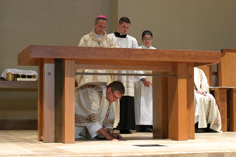 As the clergy and congregation look on, Deacon Greg Ollick places the relics of St. John Neumann from the old church in the aperture under the new altar. Photo By Michael Alexander