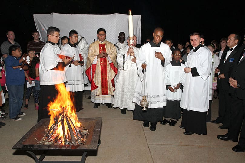 After Father Refugio Oñate Melendez, left center, pastor of St. Patrick Church, Norcross, lights the Easter Candle, Deacon José Narvaez lifts it high as they prepare to process into the church. Photo By Michael Alexander