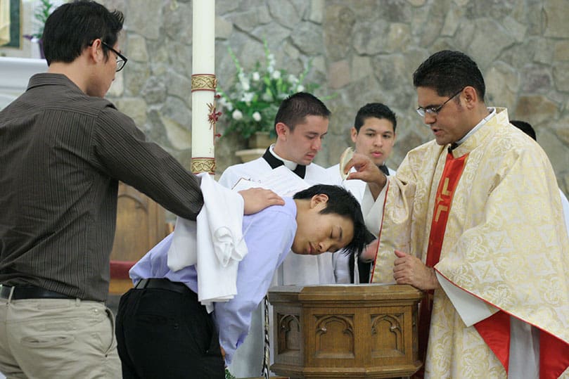 Father Refugio Oñate Melendez, right, pastor of St. Patrick Church, Norcross, baptizes catechumen Chae Yoon as his sponsor Sang Bae Chung stands behind him. Photo By Michael Alexander