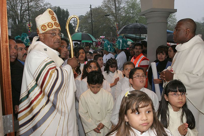 After Archbishop Wilton D. Gregory, left, unlocks the doors of the new church, a procession of altar servers and clergy make their way in as others try to get a glimpse of the interior. Photo By Michael Alexander