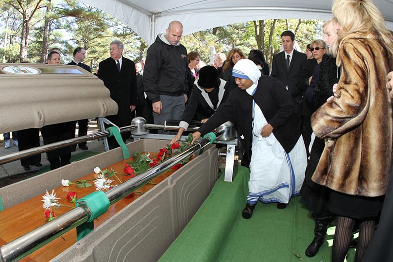 Funeral attendees place flowers on the coffin of Archbishop John F. Donoghue at the cemetery. Photo By Michael Alexander
