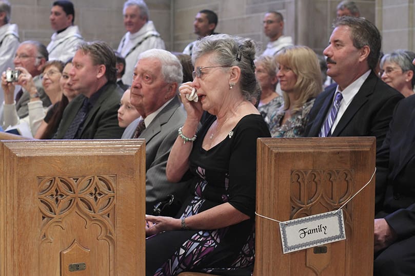 Patricia Starr, the mother of newly ordained priest Father Mark Starr, wipes away tears of joy as her son receives a sign of welcome from Archbishop Gregory and the other priests of the Atlanta Archdiocese. Seated to her right is her husband and Mark's father Richard. Photo By Michael Alexander