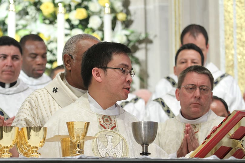 Father Tri Nguyen, center, joins his brother priests around the altar as he leads a prayer during the Liturgy of the Eucharist. Photo By Michael Alexander