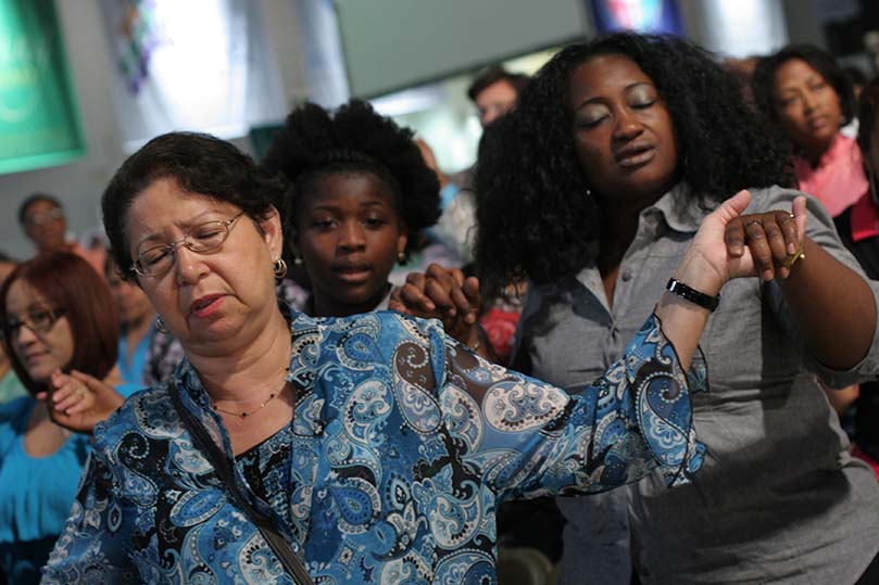 (L-r) Christ Our Hope parishioners Camille Vire, Frances Williams-Bongay and Mariatu Turay pray the Our Father during the opening Mass. Photo By Michael Alexander