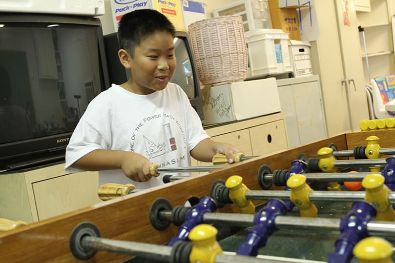 Eight-year-old Hayden Truong plays a game of foosball with a friend before morning class gets underway. The class included reading and math. Photo By Michael Alexander