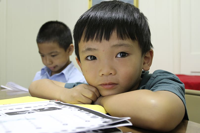 Six-year-old Jonatin Tang glances away from his educational worksheet as seven-year-old Tan Le looks over his material in the background. Photo By Michael Alexander