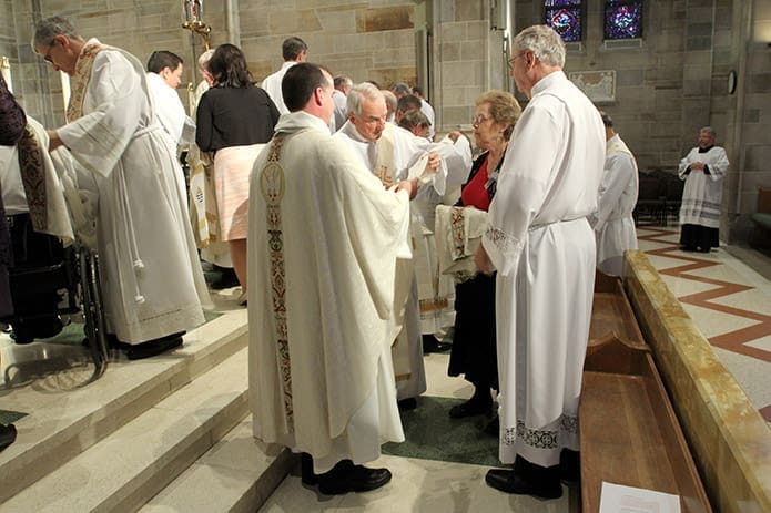 (Clockwise, from foreground left,) Father Eric Hill, pastor of Prince of Peace Church, Flowery Branch, Deacon Mike Jones, retired, and Lin Krarup stand with her husband, Paul, during the investiture with the stole and dalmatic. Photo By Michael Alexander