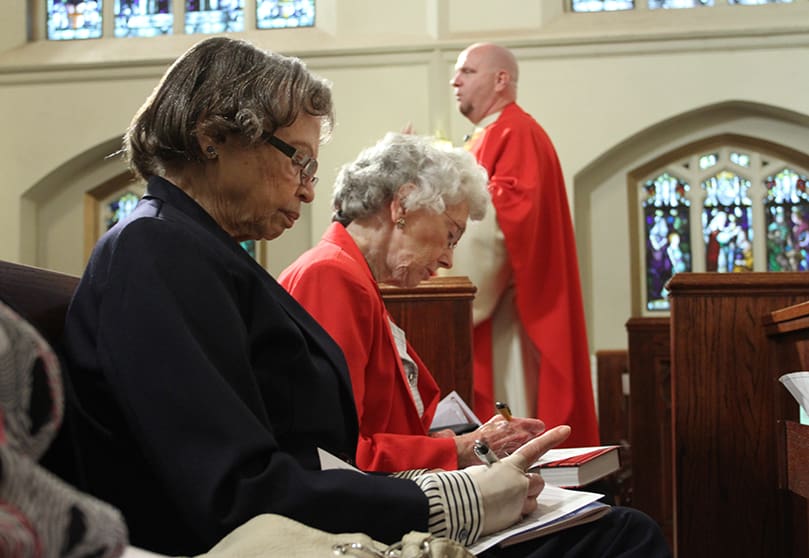 As St. Anthony of Padua Church pastor Father Victor Galier addresses the congregation on the importance of serving, the two 85-year-olds, Robinson and Todd, enthusiastically complete their Time and Talent Ministry Commitment form during Mass, May 19. Photo By Michael Alexander