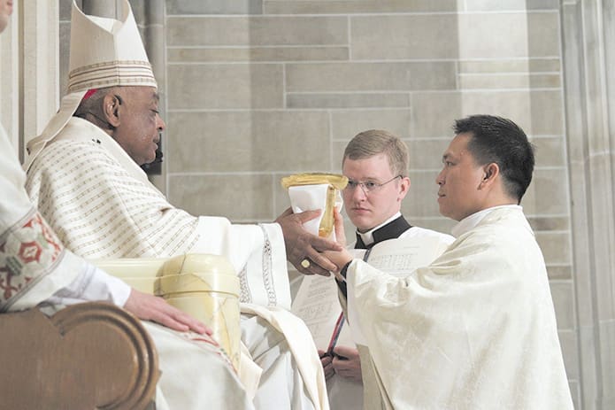 Archbishop Wilton D. Gregory presents the chalice and paten, a sign of the new priest's office, to Father Cong Nguyen. Photo By Michael Alexander