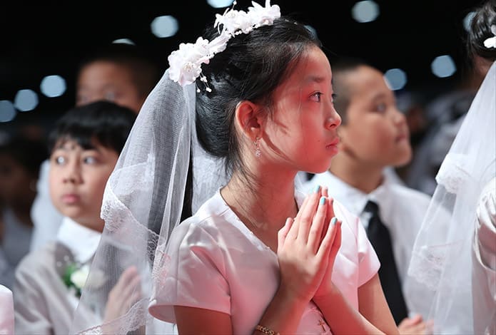 Nine-year-old Tina Tran focuses her attention toward the altar during the closing Mass of the 2014 Eucharistic Congress. Tran attends Our Lady of Vietnam Church, Riverdale. Photo By Michael Alexander