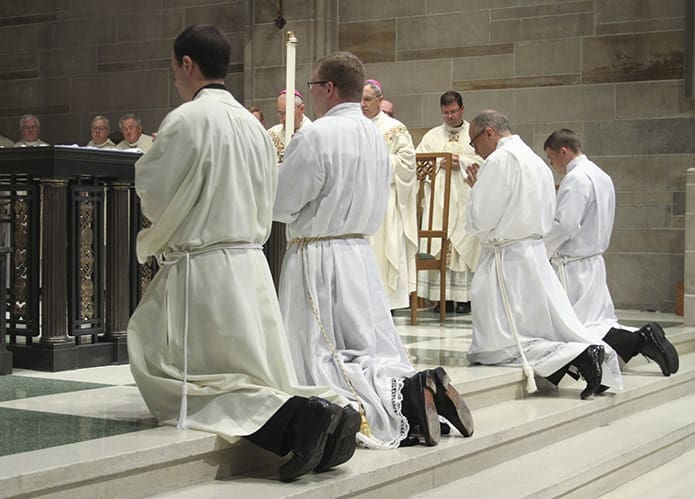 The four candidates kneel before the altar during the prayer of ordination. Photo By Michael Alexander