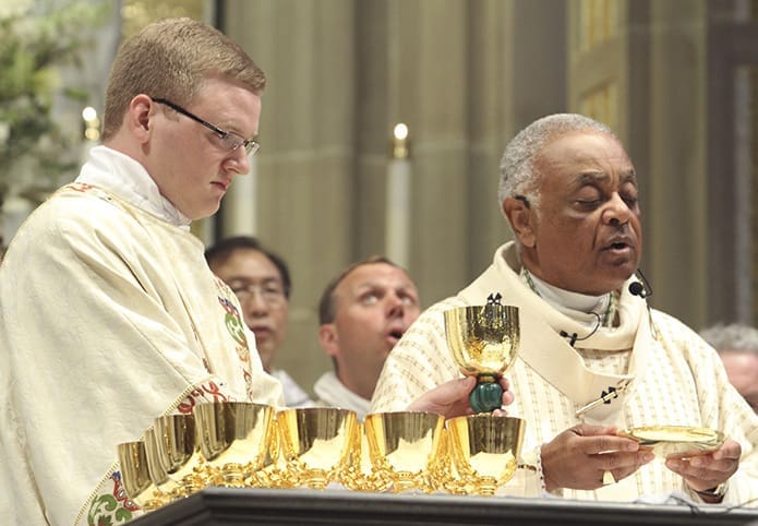 Deacon Tim Nadolski, left, elevates the chalice as Archbishop Wilton D. Gregory  elevates the paten during The Great Amen. Photo By Michael Alexander