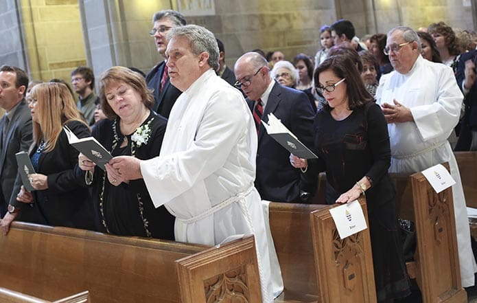 As the rite of ordination to the diaconate gets underway, candidates David Baker and Bernardo Buzeta, in white albs, stand with their respective families and invited guests. Photo By Michael Alexander