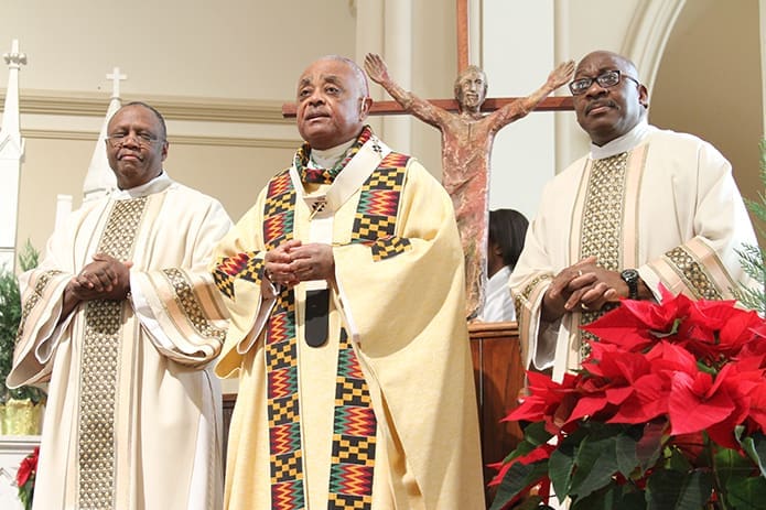 Serving on the altar with Archbishop Gregory, center, during the Mass are St. Anthony of Padua Church deacons William Simmons III, left, and Deacon Leviticus Jelks II. Photo By Michael Alexander