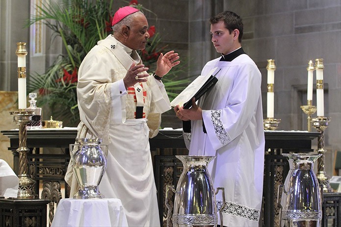Standing on the altar of the Cathedral of Christ the King, Atlanta, Archbishop Wilton D. Gregory, left, leads a prayer during the consecration of the chrism at the March 22 Chrism Mass, as seminarian Tony Ramirez holds the Roman Pontifical. Photo By Michael Alexander