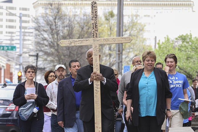 Archbishop Wilton D. Gregory, center, carries the cross from the Shrine of the Immaculate Conception to the site of the second Station of the Cross (Jesus takes up his cross), Talmadge Park, during the 36th annual Good Friday Pilgrimage through downtown Atlanta. Walking beside the archbishop is Kat Doyle, right, director of Justice and Peace Ministries. Photo By Michael Alexander