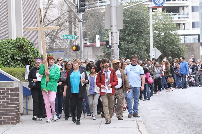 Led by Kat Doyle, foreground center, director of Justice and Peace Ministries, Joyce Wisnewski of Our Lady of the Assumption Church, Atlanta, carries the cross as they walk by Georgia State University to the site of the sixth Station of the Cross (Veronica wipes the face of Jesus), Hurt Park, during the annual Good Friday Pilgrimage through downtown Atlanta. Photo By Michael Alexander