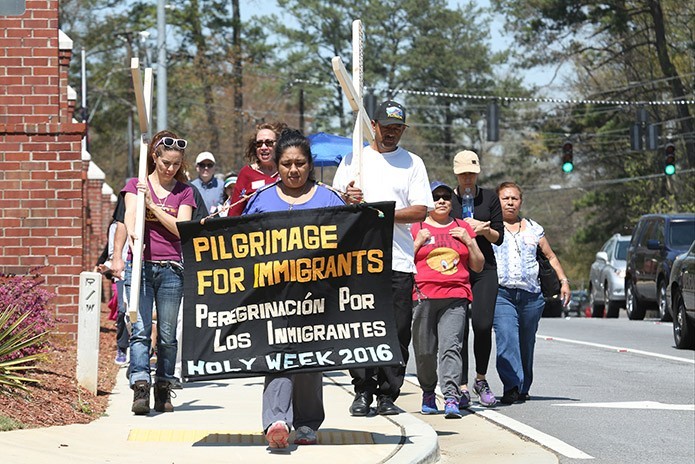 Guadalupe Robles, a native of Mexico, carries the banner as she leads a group of 25 marchers down Clairmont Road to Immaculate Heart of Mary Church, Atlanta, during the March 23 pilgrimage for immigrants, one of five conducted at various locations on different days during Holy Week. Photo By Michael Alexander