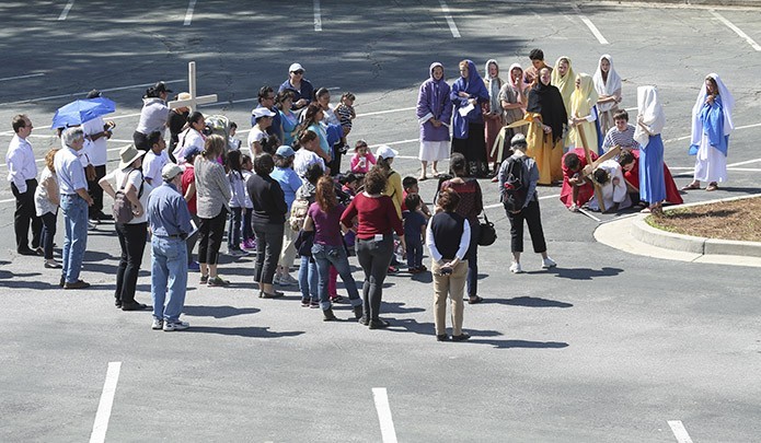 After a three-mile march from Plaza Fiesta Shopping Center to Immaculate Heart of Mary Church, Pilgrimage for Immigrants marchers watch as Immaculate Heart of Mary School seventh graders illustrate the ninth Station of the Cross (Jesus falls the third time) in the church’s lower parking lot. The version of the stations performed by the students was based on the Gospel of Luke. Photo By Michael Alexander