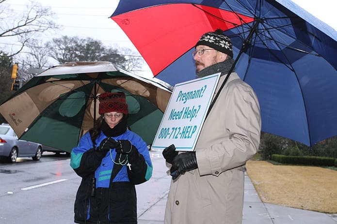 Standing on Peachtree Road during Stand for Life, Christine and Edward Kujawski of St. Brigid Church in Johns Creek pray the rosary in the pouring rain. Photo By Michael Alexander