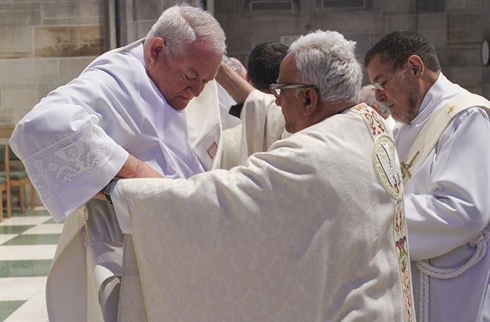 (R-l) Deacon Ed Rademacher of St. Monica Church, Duluth, and Missionary of St. Frances de Sales Father Joseph Mendes vest permanent diaconate candidate Jack Herndon with his stole and dalmatic. Photo By Michael Alexander