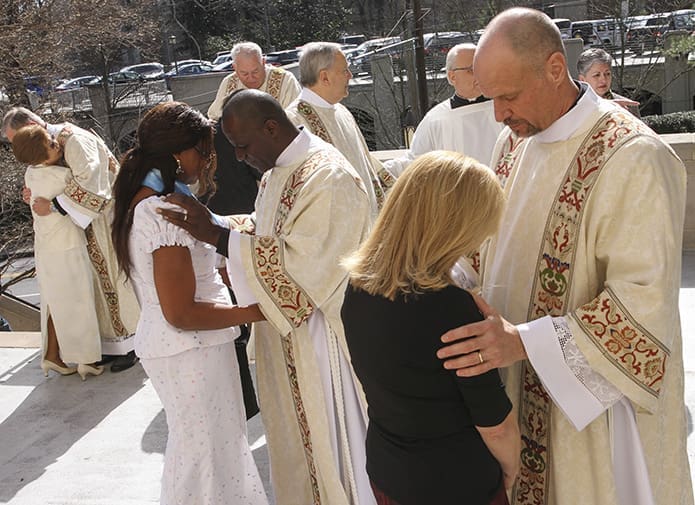 Standing on the Cathedral of Christ the King plaza following the ordination, (r-l) Deacon Paul Schueth of Good Samaritan Church, Ellijay, extends a blessing to his wife Betsy, Deacon Kapya Muzinga Ngoy of Saint Marguerite D'Youville Church, Lawrenceville, does the same for his wife Mwisangie, and Deacon Julian Peter Harris receives a congratulatory hug from his wife Kyong Ok. Photo By Michael Alexander