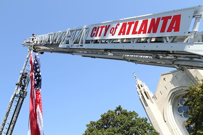 After attaching the American flag to the fire truck ladders, Atlanta firemen Sgt. Kent Thornton, left, and Patrick McNeil make their way down from high above Peachtree Way in front of the Cathedral of Christ the King. Photo By Michael Alexander
